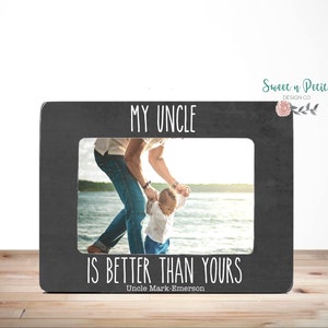 Puede incluir: Un marco de fotos negro con un borde blanco y el texto "MY UNCLE IS BETTER THAN YOURS" y "Uncle Mark-Emerson". El marco tiene una foto de un hombre adulto y un niño pequeño en una playa.