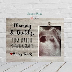 May include: A white wood frame with a black and white ultrasound image of a baby. The text "Mommy & Daddy, I love you both so much already! Baby Davis" is written on the frame.