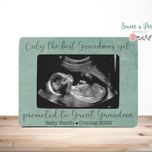 Puede incluir: Un marco de fotos azul verdoso con fondo blanco y el texto "Only the best Grandmas get promoted to Great Grandma Baby Smith Coming 2022". El marco tiene una imagen de ultrasonido en blanco y negro en su interior.