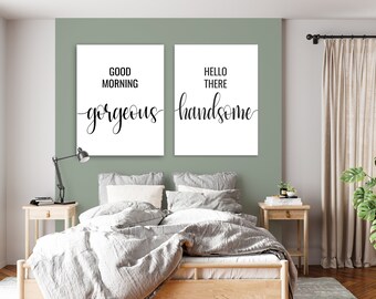 May include: Two framed prints with black calligraphy on a white background. The left print says "Good Morning Gorgeous" and the right print says "Hello There Handsome". The prints are hanging on a sage green wall above a bed with white bedding.