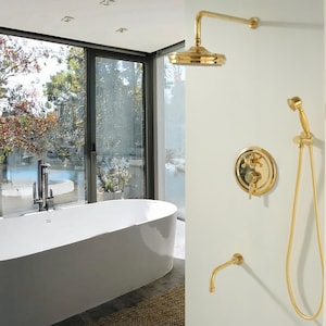 May include: A bathroom featuring a white oval bathtub and a large window with a view of greenery. The wall displays gold-coloured shower fixtures, including a showerhead, faucet, and handheld shower. The fixtures have a classic design.