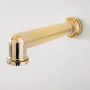Pode incluir: Uma torneira dourada com um design em &acirc;ngulo reto. A torneira &eacute; montada numa superf&iacute;cie branca. A torneira tem um corpo cil&iacute;ndrico e uma base circular.