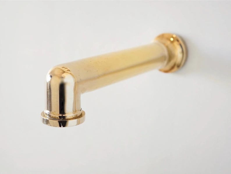 Pode incluir: Uma torneira dourada com um design em &acirc;ngulo reto. A torneira &eacute; montada numa superf&iacute;cie branca. A torneira tem um corpo cil&iacute;ndrico e uma base circular.