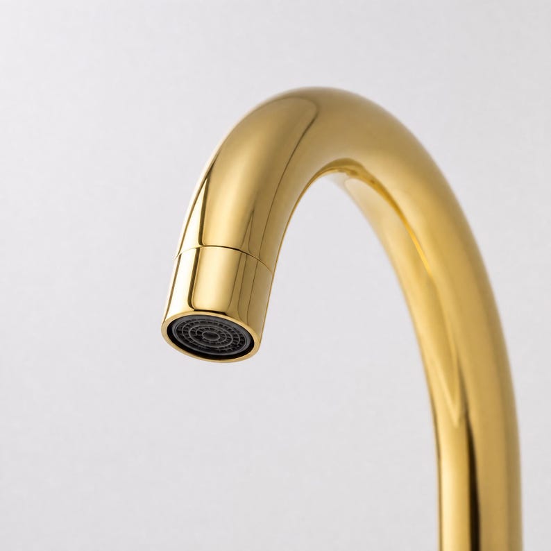 May include: Close-up of a gold-colored faucet with a curved spout. The faucet has a shiny finish and a black aerator at the end of the spout. The background is plain white.