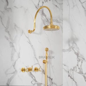 May include: Gold-colored shower fixture set against a white marble wall. The set includes a rain shower head, handheld shower, and faucet controls. The brand name "BRASSLIK" is visible.