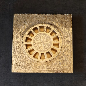 Könnte beinhalten: Ein quadratischer Abflussdeckel aus Messing mit einem filigranen Blumendesign und einem runden Gitter in der Mitte.