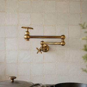 Könnte beinhalten: Ein wandmontierter Topffüller-Wasserhahn mit Messing-Finish, ausgestattet mit einem doppelt gelenkigen Arm und zwei Kreuzgriffen. Die Armatur hat ein metallisch poliertes Aussehen mit abgerundeten Gelenken und einem horizontalen Design.