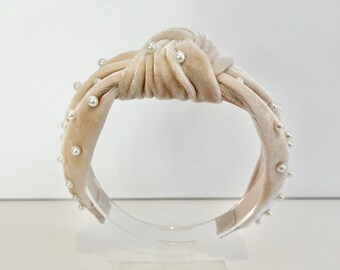 May include: A cream-colored velvet headband with a knotted design and pearl embellishments.