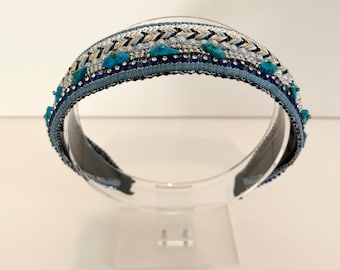 Puede incluir: Una diadema azul con un diseño de cuentas con detalles en turquesa y plata. La diadema está sobre un fondo blanco.