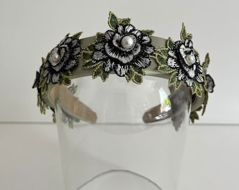 Puede incluir: Una diadema verde con flores bordadas en blanco y negro y detalles de perlas.