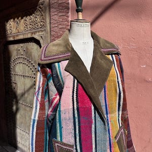 May include: A vibrant patchwork coat with a corduroy collar and pockets. The coat showcases vertical stripes in pink, blue, yellow, and brown. The coat is displayed on a mannequin.