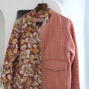 May include: A two-toned bomber jacket. One side features a burgundy floral pattern with cream and yellow flowers. The other side is a textured pink fabric with a pocket. The jacket has a zipper closure.