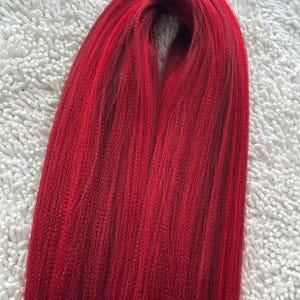 May include: A bundle of long, straight, red synthetic hair extensions.