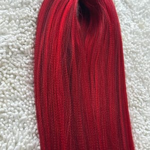 May include: A bundle of long, straight, red hair extensions. The hair is smooth and shiny.