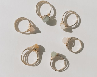 Puede incluir: Seis anillos de oro con piedras de diferentes colores. Los anillos están hechos de alambre envuelto alrededor de las piedras. Las piedras son verdes, rosas, amarillas y blancas.