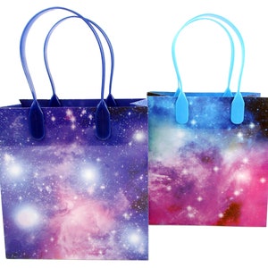 May include: Two galaxy-themed gift bags with blue handles. The bags have a purple and pink galaxy print with white stars.