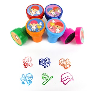 May include: Set of six colorful plastic stamps featuring baseball-themed illustrations. The stamps are arranged in a circle on a white background. The illustrations include a baseball player, a baseball glove, a baseball bat, and a baseball cap. The stamps are all different colors, including red, blue, green, orange, and pink.