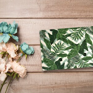 May include: A green and white patterned gift wrap with a tropical leaf design. The wrapping paper features a chevron pattern and green leaves.