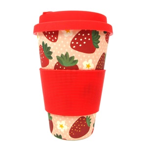 Peut inclure: Une tasse à café réutilisable rouge et blanche avec un motif de fraises. La tasse a une gaine en silicone rouge.