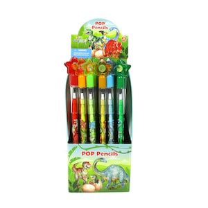 Könnte beinhalten: Eine Auslage mit acht bunten Pop-Stiften mit Dinosaurier-Motiven. Die Stifte haben sternförmige Aufsätze und sind in einer Schachtel mit einer Dinosaurier-Illustration und dem Text "POP Pencils" verpackt.