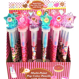 Puede incluir: Una caja de exposición de 24 lápices multi-point pop de colores con temática de donuts. Los lápices tienen una parte superior en forma de estrella con un diseño de donut y un barril de plástico transparente con un patrón de donut. La caja tiene un fondo a rayas rosa y marrón con ilustraciones de donuts.