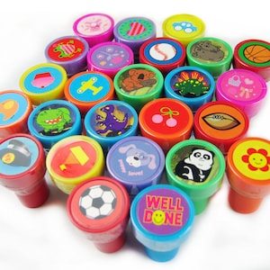Puede incluir: Una colección de 24 sellos de goma de colores con varios diseños, incluyendo animales, deportes y palabras. Los sellos están dispuestos en un círculo sobre un fondo blanco.