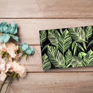 May include: A rectangular card with a tropical leaf pattern. The leaves are green and white on a black background.