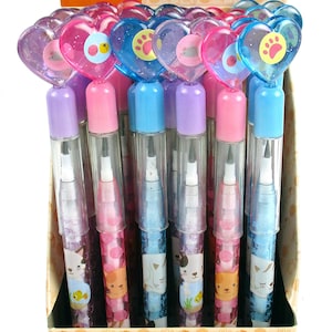 May include: A box of 24 pop pencils with heart-shaped toppers. The pencils are clear with glitter and feature cute cat designs. The box is pink and yellow with a cat illustration and the text "Pop Pencils".