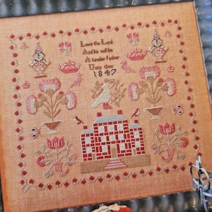 May include: A beige cross-stitch sampler with a red brick house, flowers, and birds. The text reads "Love the Lord and he will be a tender father unto thee 1847".