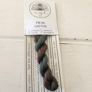 May include: A skein of hand-dyed stranded cotton embroidery floss in shades of green and brown. The floss is labelled "PB 05 Cactus" and is 100% cotton. It is 10 metres long and comes in 50 cm lengths.