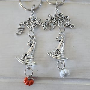 Puede incluir: Dos llaveros plateados con un dije de sombrero de bruja de metal con estrellas recortadas, un conector de nudo celta, un pequeño dije de bruja en escoba y un dije de calabaza en miniatura, uno naranja y otro blanco, en una argolla.
