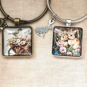 Può includere: Due bracciali circolari in metallo con pendenti quadrati. Il bracciale color bronzo ha un ciondolo a forma di lumaca e un pendente con un uccellino su un carretto di legno fiorito. Il bracciale argentato ha un ciondolo a forma di coniglio e due conigli.