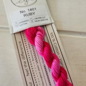 Pode incluir: Um novelo de linha de bordar de algodão torcido na cor rubi. O rótulo diz "Nº 1401 Ruby" e "10M pré-cortado, comprimentos de 50cm". A linha é um gradiente de rosa e vermelho. A embalagem inclui exemplos de pontos.