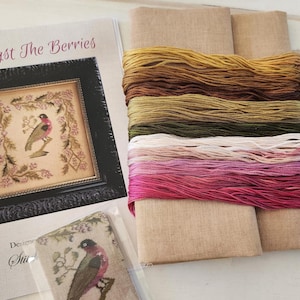May include: Cross-stitch kit with a framed bird design, floral border, and the title "Amongst The Berries". The kit includes coloured threads, fabric, and a pattern. The threads are in shades of pink, green, and brown.
