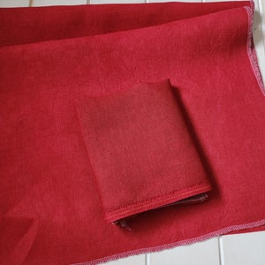 May include: Two pieces of red fabric with a slightly textured surface. The fabric is folded and has a stitched edge.