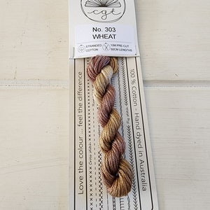 May include: A skein of stranded cotton embroidery floss in shades of brown, beige, and gold. The floss is labeled "No. 303 WHEAT" and is 100% cotton, hand-dyed in Australia. The floss is pre-cut into 50 cm lengths.