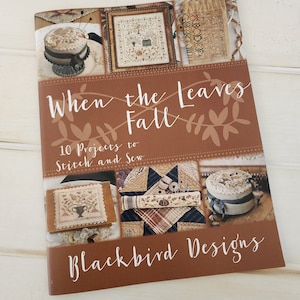 May include: A book titled "When the Leaves Fall" with a brown cover featuring a variety of cross-stitch projects. The book is by Blackbird Designs and features 10 projects to stitch and sew.