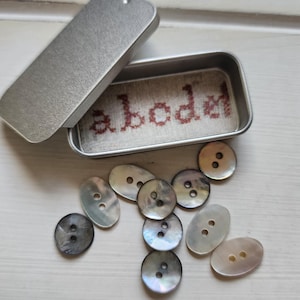 Piccola scatola di latta con 10 bottoni a conchiglia