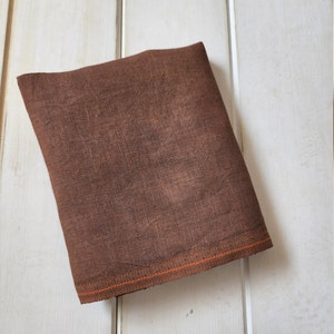 May include: A brown fabric swatch with an orange stitched edge. The fabric has a textured, linen-like appearance.