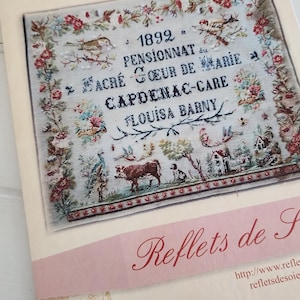 May include: A printed pattern booklet titled Louisa Barny 1892 featuring a cross-stitch sampler design. The sampler includes floral borders, birds, a cow, a dog, and text reading 1892 PENSIONNAT du SACRE COEUR DE MARIE CAPDENAC-GARE LOUISA BARNY.