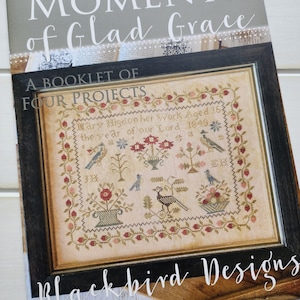 Puede incluir: Un folleto titulado "Moments of Glad Grace" que presenta cuatro proyectos de bordado de punto de cruz. La portada muestra un diseño de punto de cruz enmarcado con un motivo floral, pájaros y el texto "Mary Higdon her Work Aged 16: the year of our Lord 1849." El folleto es de Blackbird Designs.