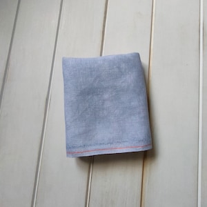 May include: A light blue fabric square with a red stitched border. The fabric has a subtle texture.
