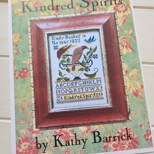 Puede incluir: Un patrón de punto de cruz titulado "Kindred Spirits" de Kathy Barrick. El patrón presenta un pájaro en un tazón con un diseño floral y el texto "Emily Bookex in the year 1822".