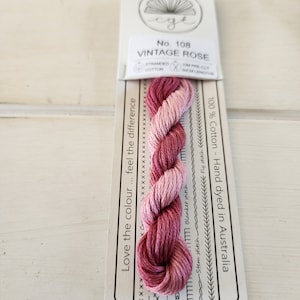 May include: A skein of hand-dyed stranded cotton embroidery floss in shades of pink and red. The floss is labeled "Vintage Rose" and "No. 108". The label also states "100% Cotton - Hand dyed in Australia".