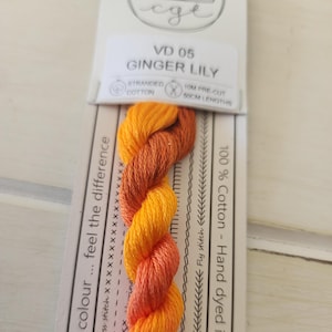 May include: A skein of stranded cotton embroidery floss in shades of orange, yellow, and red. The floss is labeled "VD 05 Ginger Lily" and is 100% cotton, hand-dyed, and pre-cut into 50cm lengths.