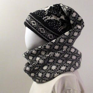 Puede incluir: Conjunto de gorro y bufanda de punto negro y blanco con un patrón geométrico. El gorro tiene un puño abatible y la bufanda es de estilo cuello.