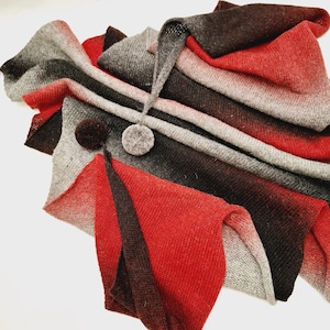 May include: A red, grey, and black ombre knitted scarf with a grey pom-pom on the end.