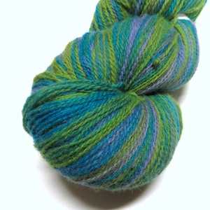 Puede incluir: Un ovillo de hilo en tonos de verde, azul y morado. El hilo está retorcido en forma de espiral.