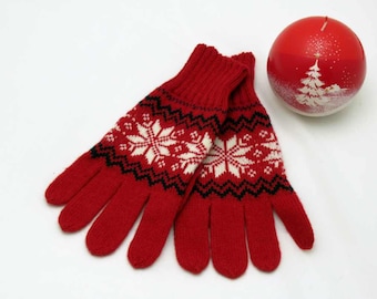 May include: Red knitted gloves with a white snowflake pattern and black trim. The gloves are folded together and are on a white background.