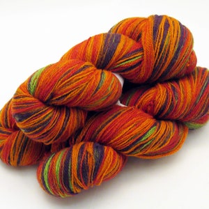 Puede incluir: Un ovillo de hilo en un patrón multicolor de naranja, rojo, verde y morado. El hilo está retorcido y doblado en forma de bola.